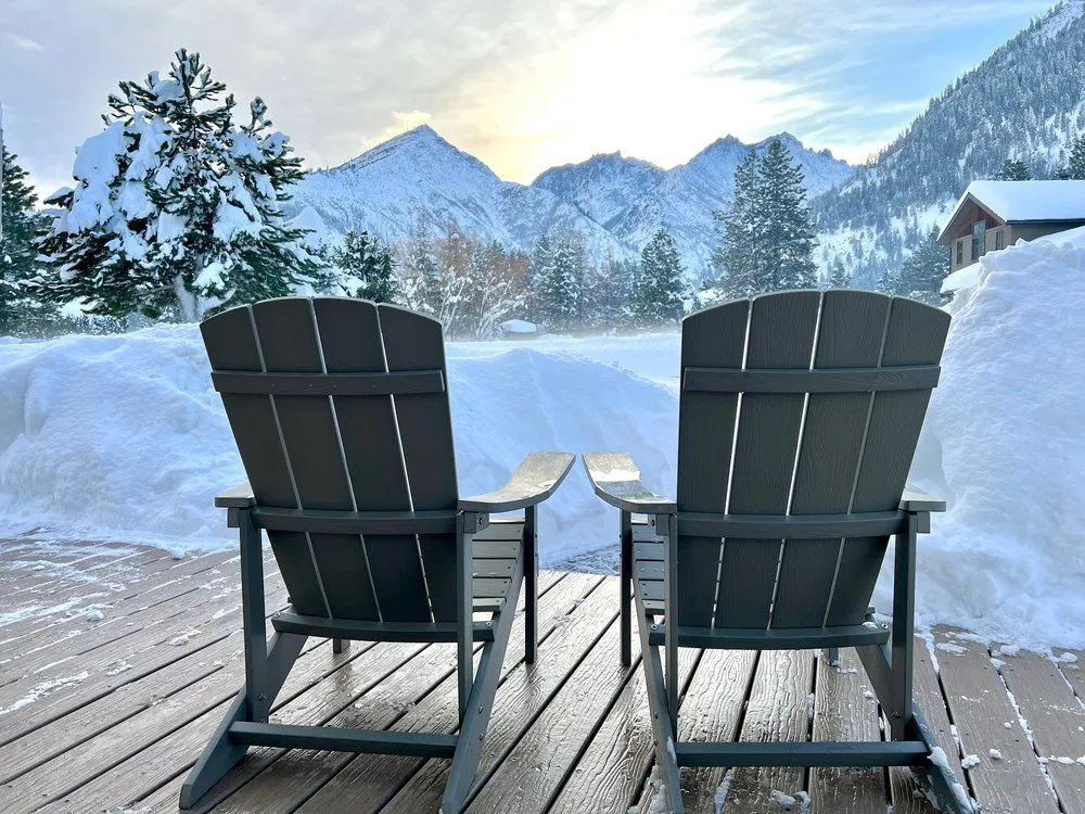 Two Adirondack chairs on the deck facing snow-covered mountains and evergreens at sunrise in Leavenworth