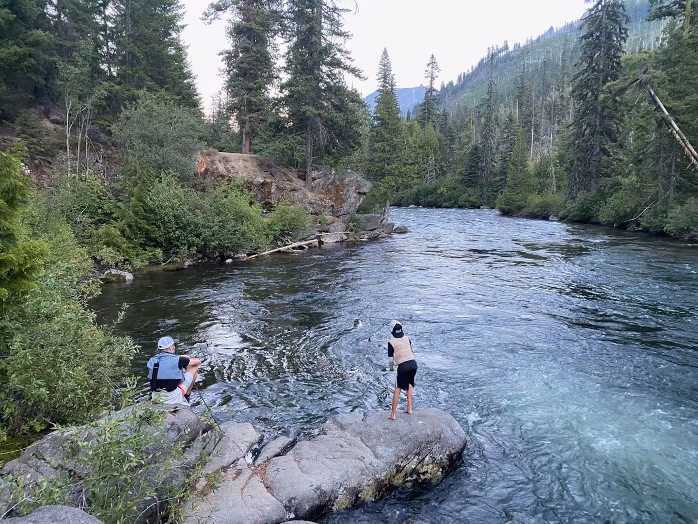 A father and son on granite boulders beside the clear green water of Icicle Creek in summer