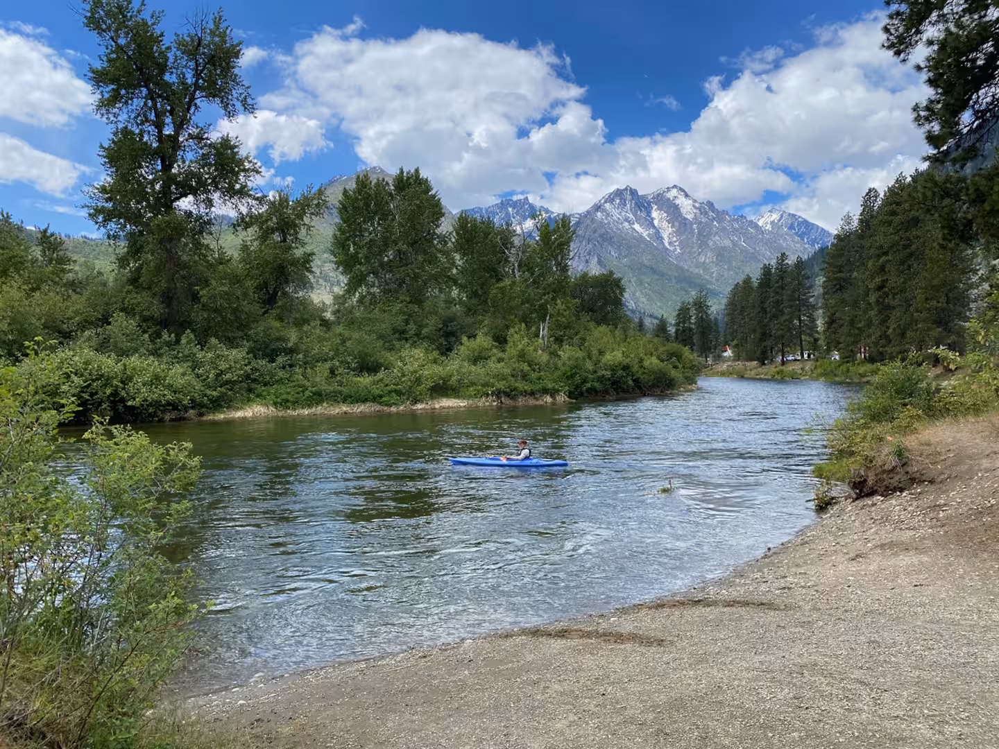 A kayaker paddling a calm stretch of river below snow-streaked Cascade peaks near Leavenworth