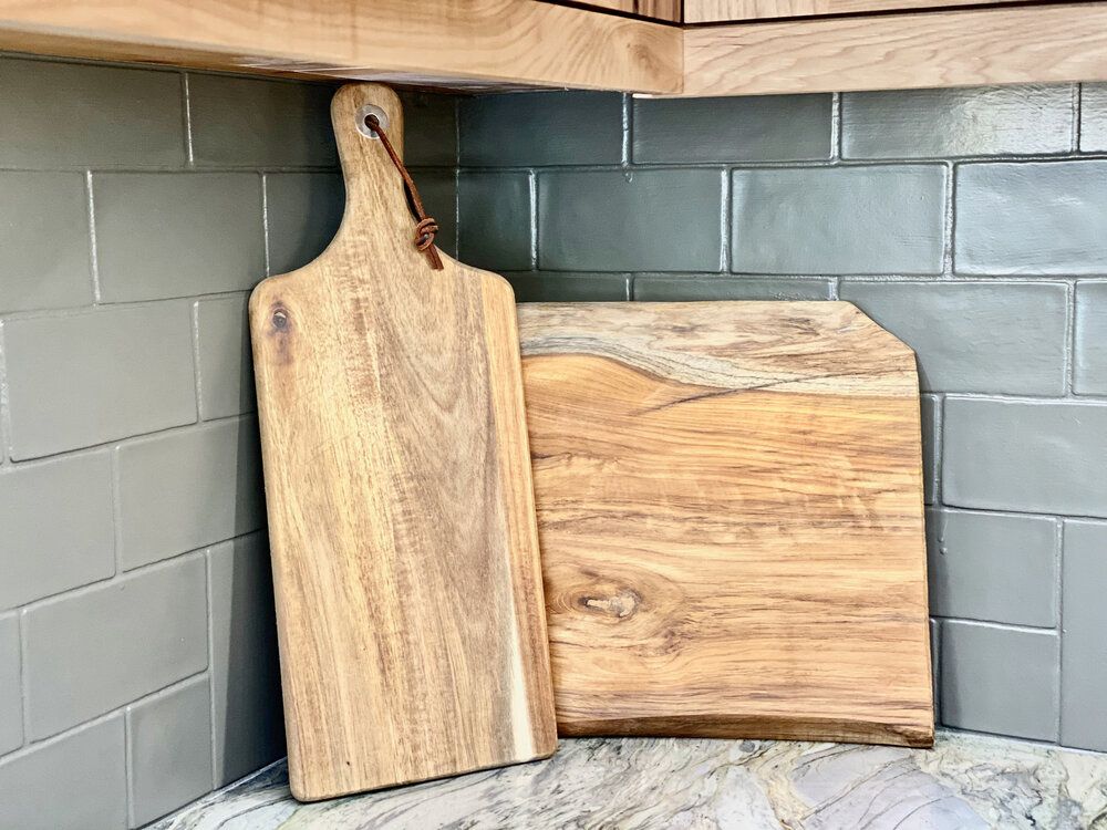 Wooden serving and cutting boards leaning against the grey tiled backsplash in the kitchen