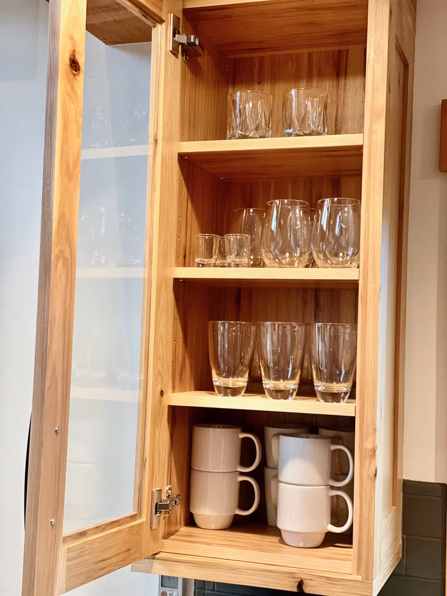Hickory cabinet stocked with wine glasses, tumblers and stacked mugs in the kitchen at The Cascade Chalet