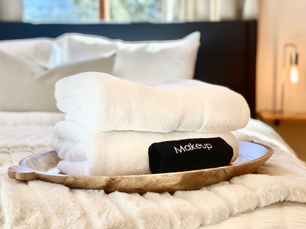 Rolled white towels and a makeup towel set out on a wooden tray on the bed
