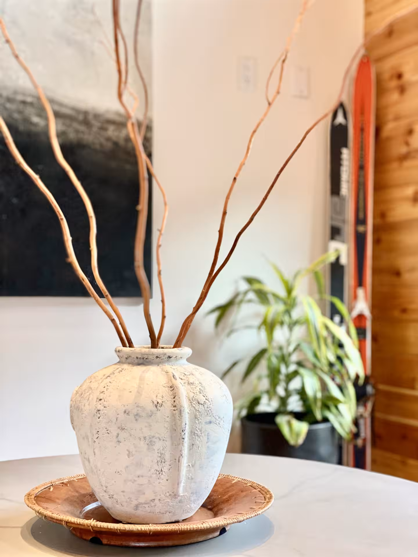 Round marble dining table with a stoneware vase of curly willow branches, vintage skis on the cedar wall behind