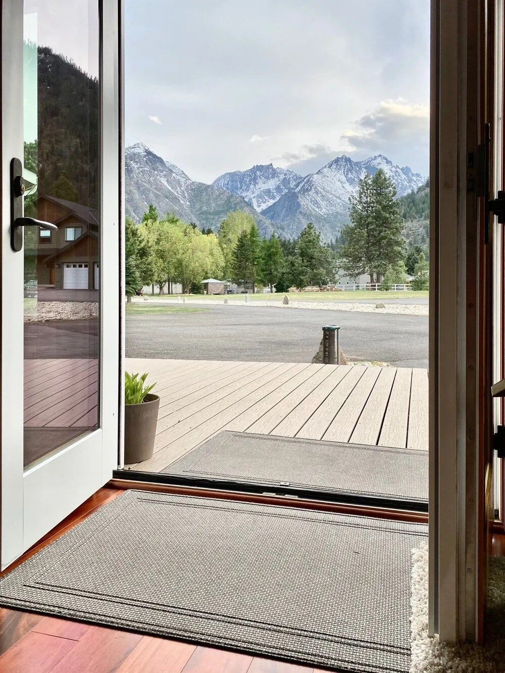 Open french doors in the great room looking past the deck to snow-capped Cascade peaks and evergreens