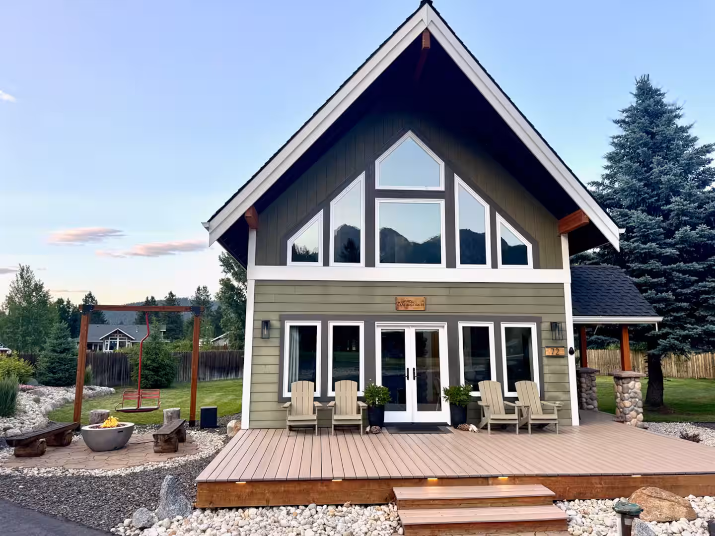 The Cascade Chalet vacation rental in Leavenworth WA at dusk: gabled A-frame with a wall of windows, Adirondack chairs on the deck and the ski lift swing on the lawn