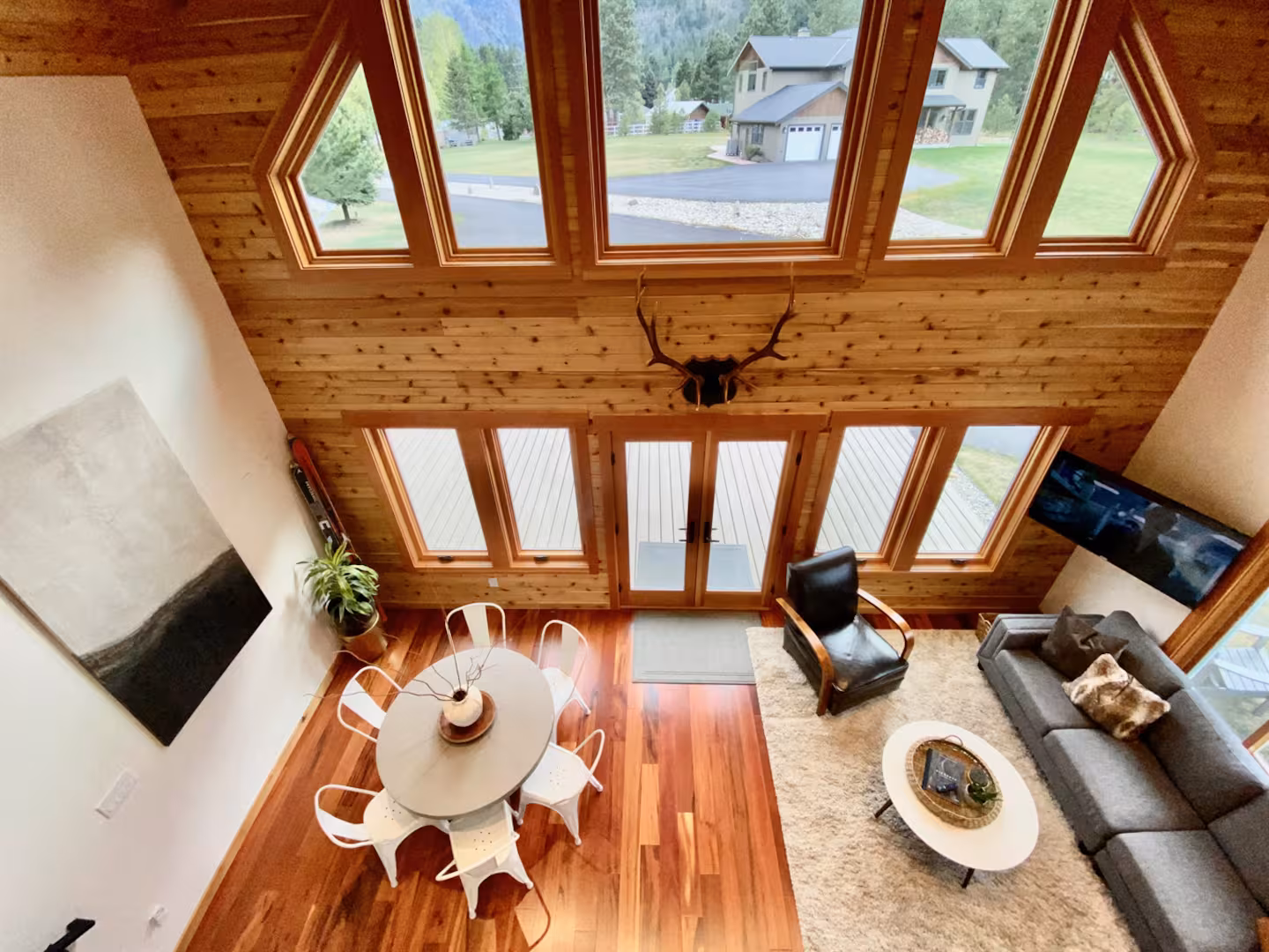The great room seen from the loft: vaulted cedar ceiling, diamond gable windows, dining table and sectional sofa below