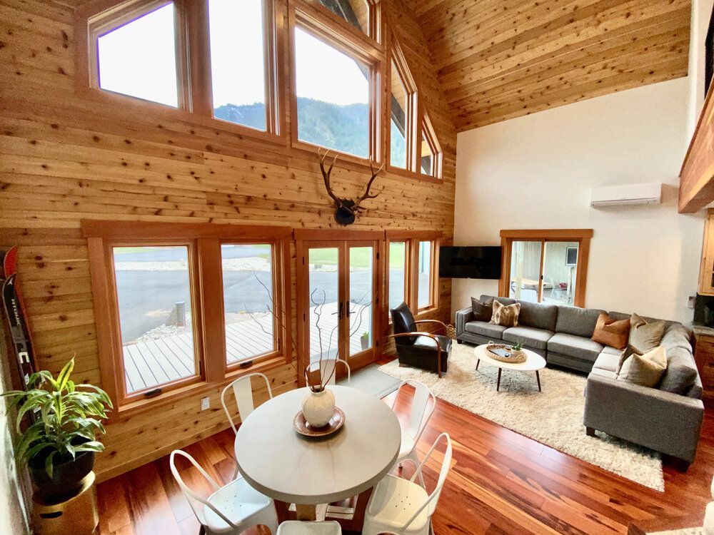 Open living and dining area with sectional sofa, round dining table and a wall of windows facing Wedge Mountain