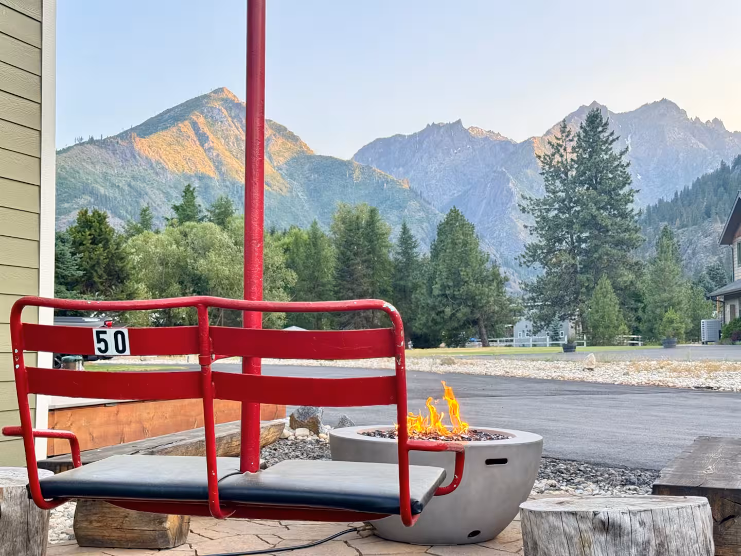 Vintage red chair 50 ski lift swing beside the lit gas fire pit at The Cascade Chalet, facing alpenglow on the Cascade peaks