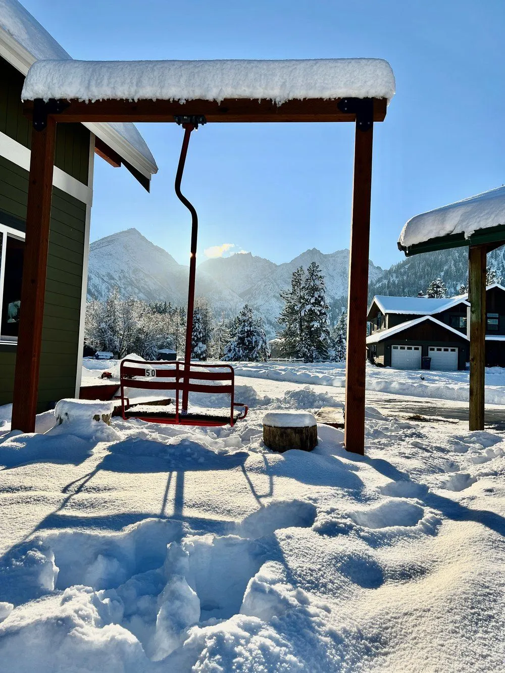 The vintage red chair 50 ski lift swing under a snow-covered pergola with sun rising over the snowy Cascade peaks